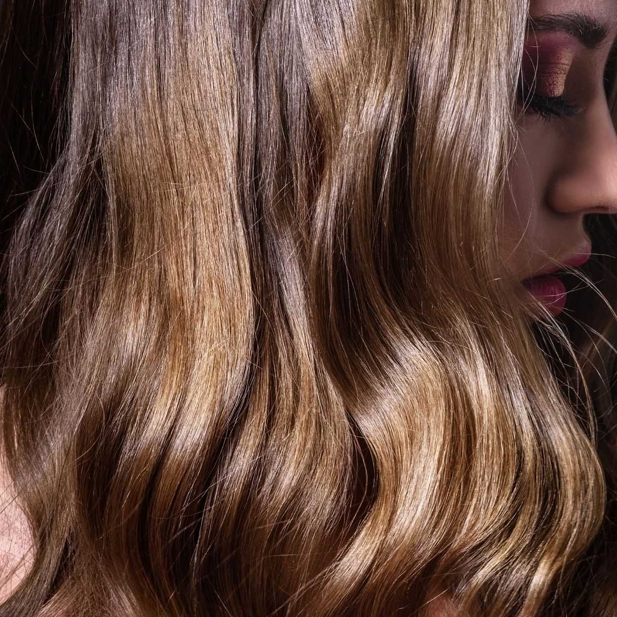 Close-up of woman with wavy brown hair, focusing on the texture and natural highlights.